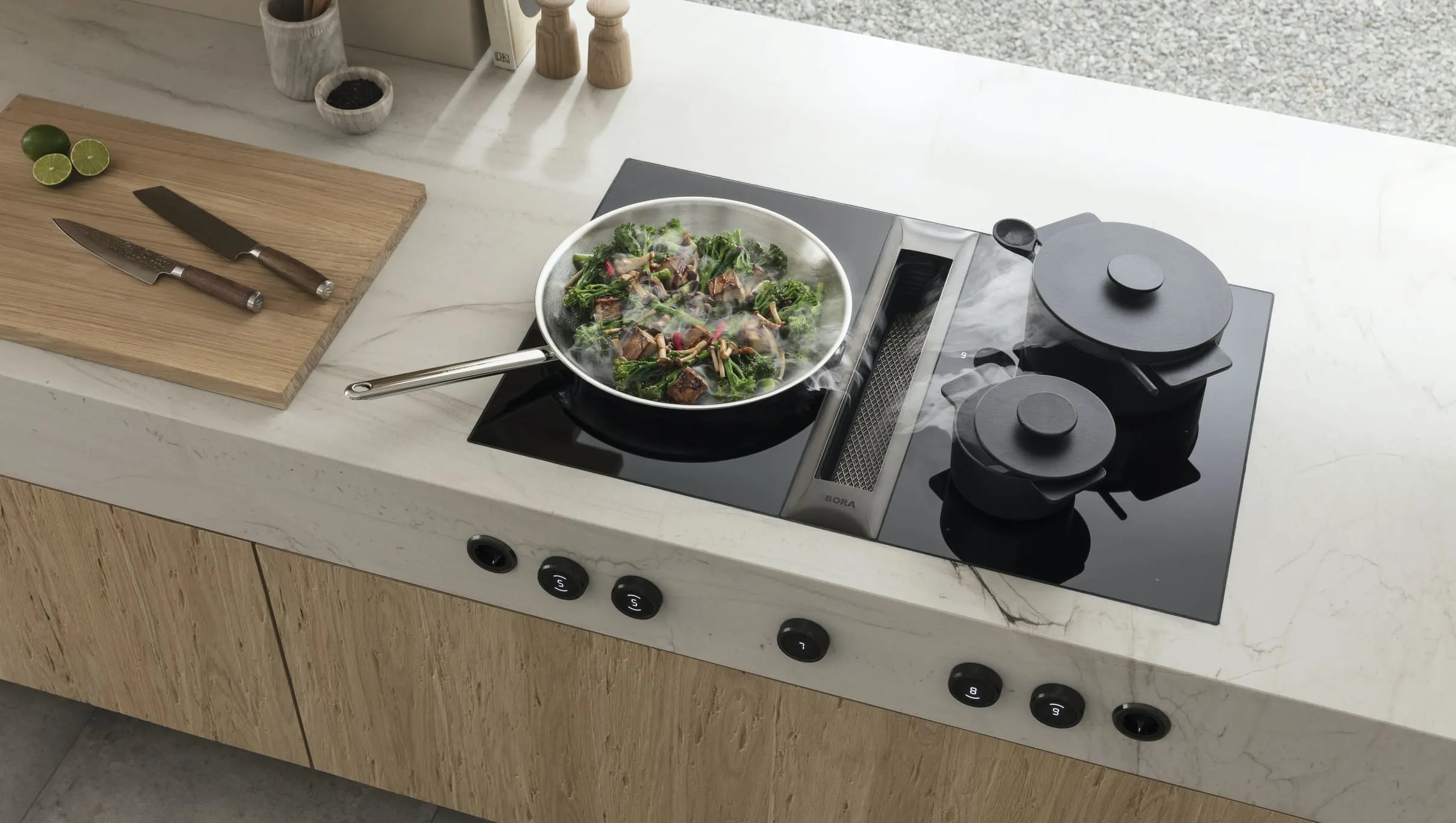 2 (1) Kuhinja u svetlim tonovima sa BORA Professional 3.0 aspiratorom i pločama – priprema jela uz prirodno osvetljenje i minimalističan enterijer.