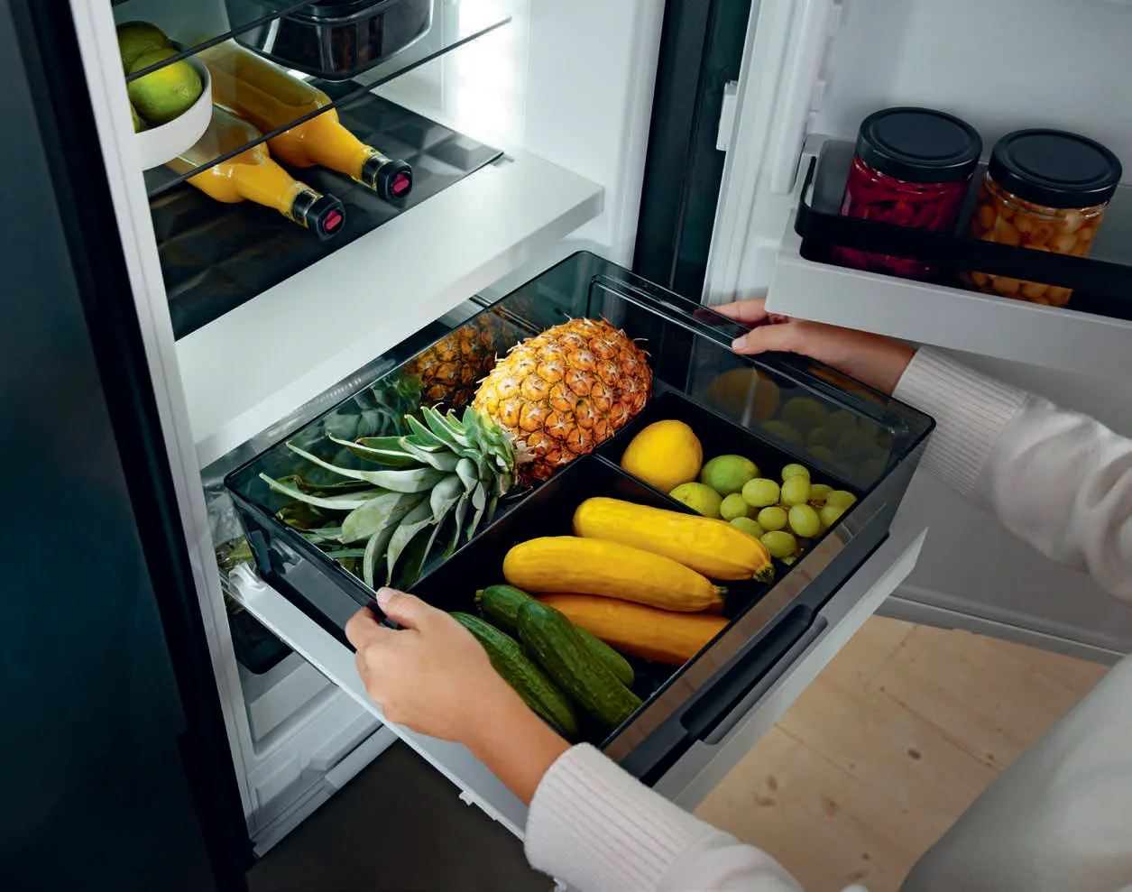 5 Unutrašnjost BORA Cool frižidera sa policama od stakla i posudama sa voćem, povrćem i napicima, uz osvetljenje koje naglašava dizajn.