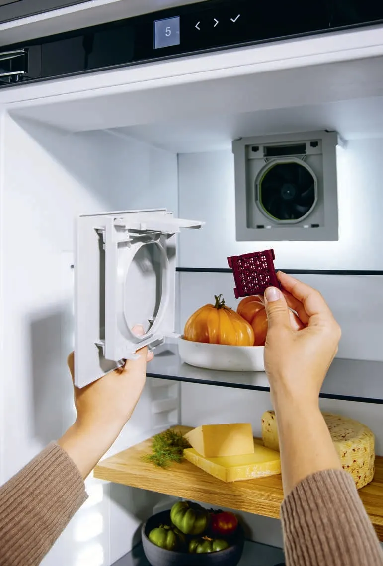 9 Zamena filtera u BORA Cool frižideru – ruke ubacuju element filtera za mirise ispred police sa paradajzom i sirom.