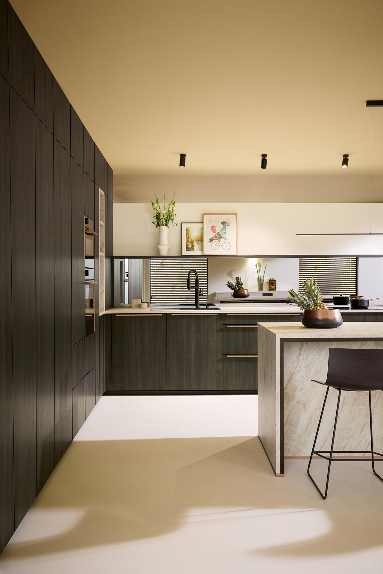 VAR-K833_GS_2026 Bočni pogled na Schüller Varese kuhinju, koji ističe kontrast tamnog Sijena hrasta, mermernog ostrva i reflektujuće niše od ogledalo stakla.