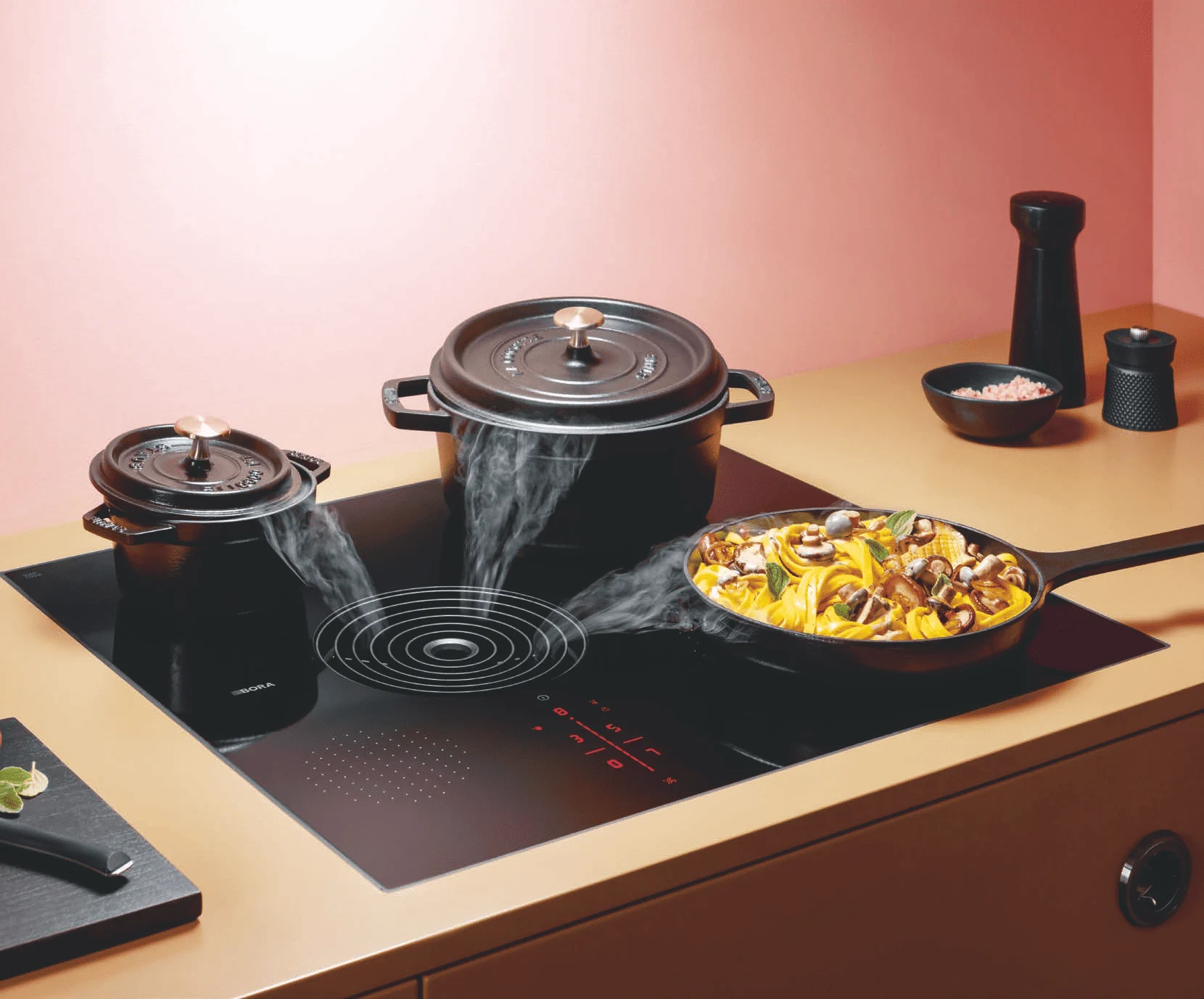 at1dndzua1gk8qwuwyu0 BORA S Pure ploča za kuvanje u elegantnoj zlatnoj kuhinji, sa crnim posuđem i integrisanim aspiratorom koji nežno uvlači paru tokom pripreme obroka.