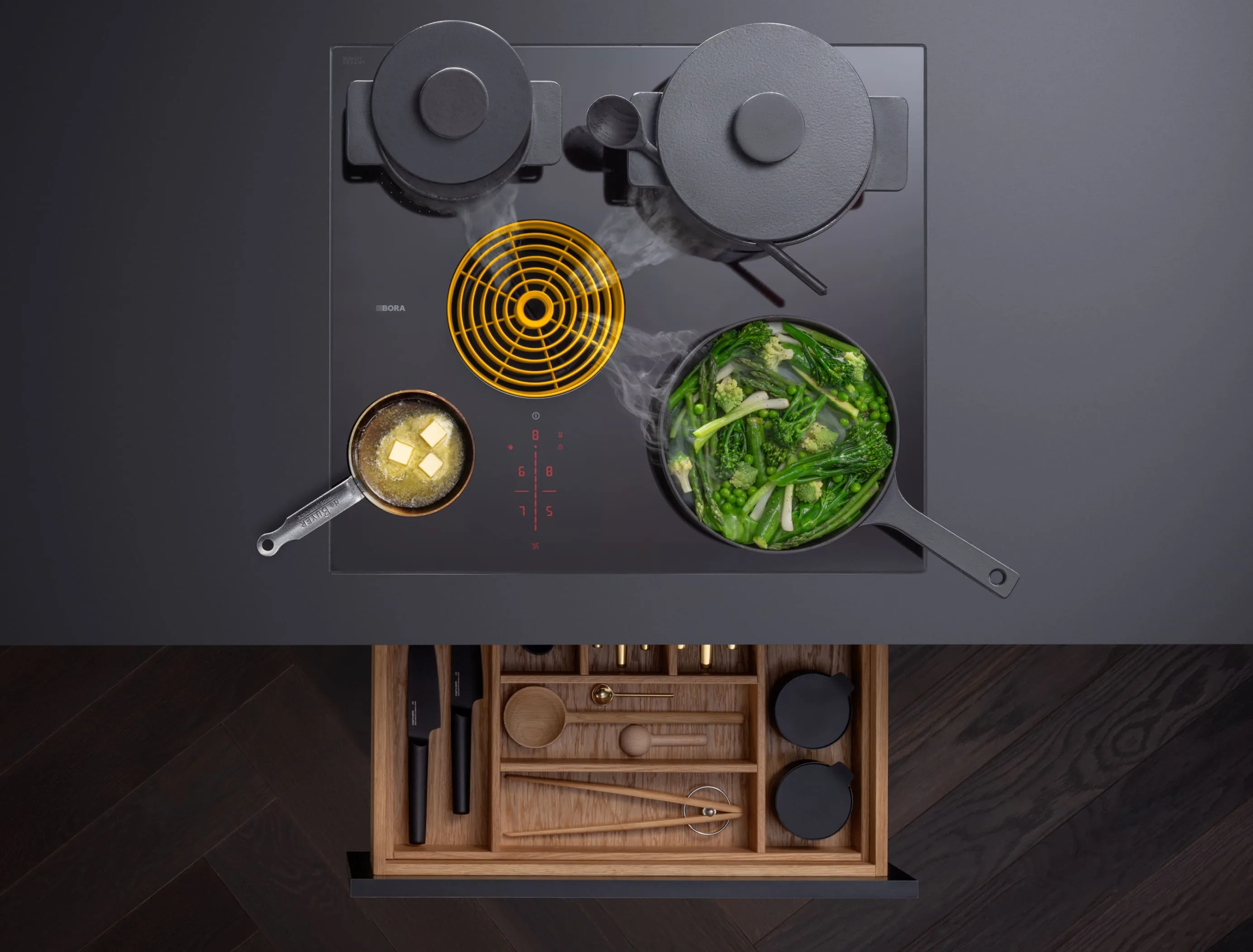 mkrjhuhkr6j79rsz2gf6 Pogled odozgo na BORA S Pure ploču sa žutim ventilacionim otvorom i više lonaca tokom kuvanja na različitim zonama.