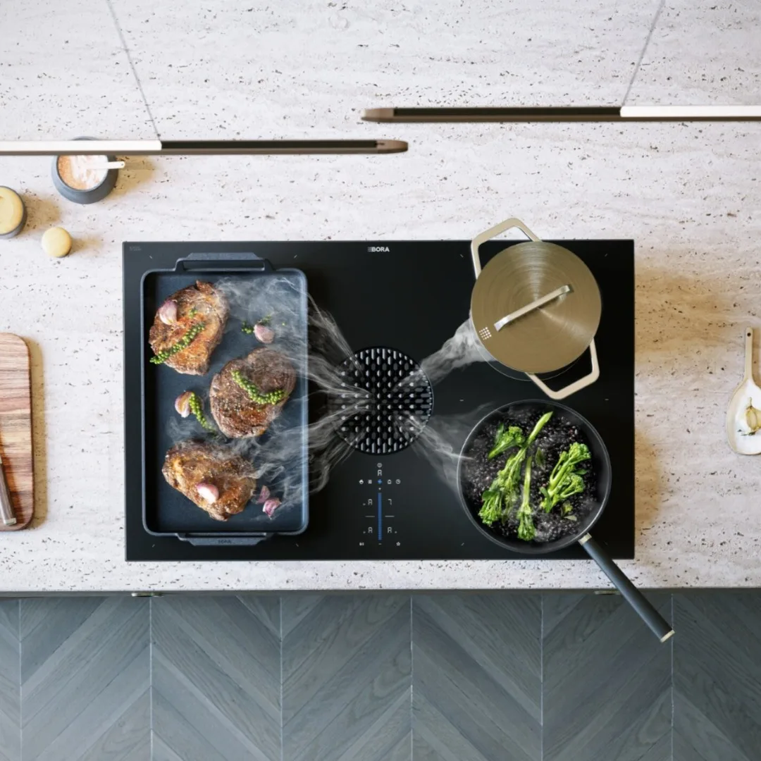 rwxs1q9vmy52rdnhnd6c Pogled odozgo na BORA X Pure ploču sa tri posude i integrisanom aspiracijom koja uvlači paru u prepoznatljivu crnu mlaznicu u sredini.